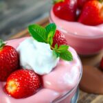 strawberry pudding :Two dessert bowls filled with pink yogurt topped with strawberries and mint leaves sit on a wooden tray.